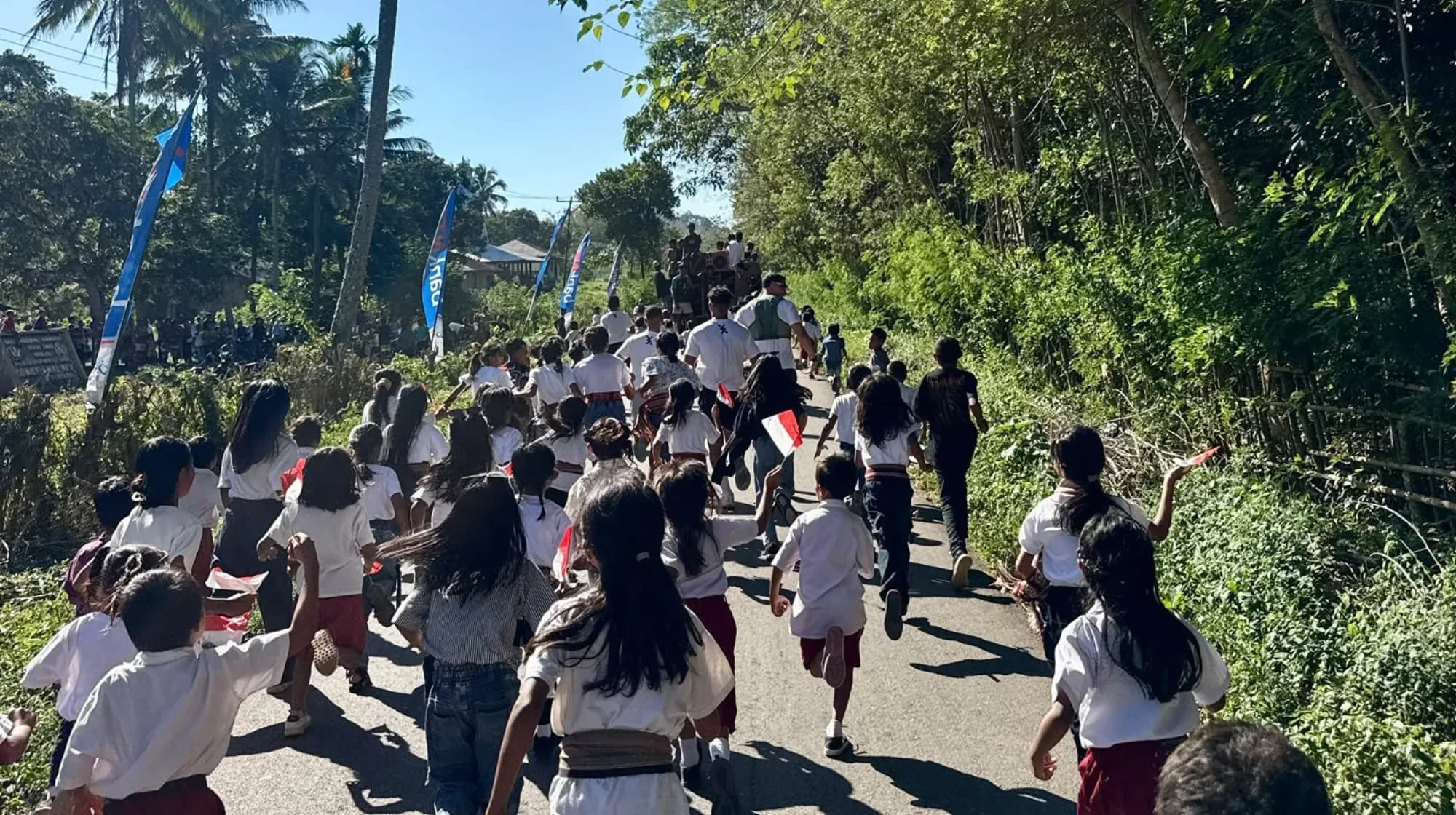 Anak-anak sekolah berseragam putih merah berlari menjauh di jalan desa di Sumba.